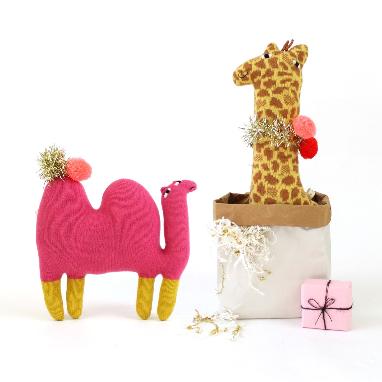 Pink knitted camel and giraffe plush toys with decorative elements on a white background