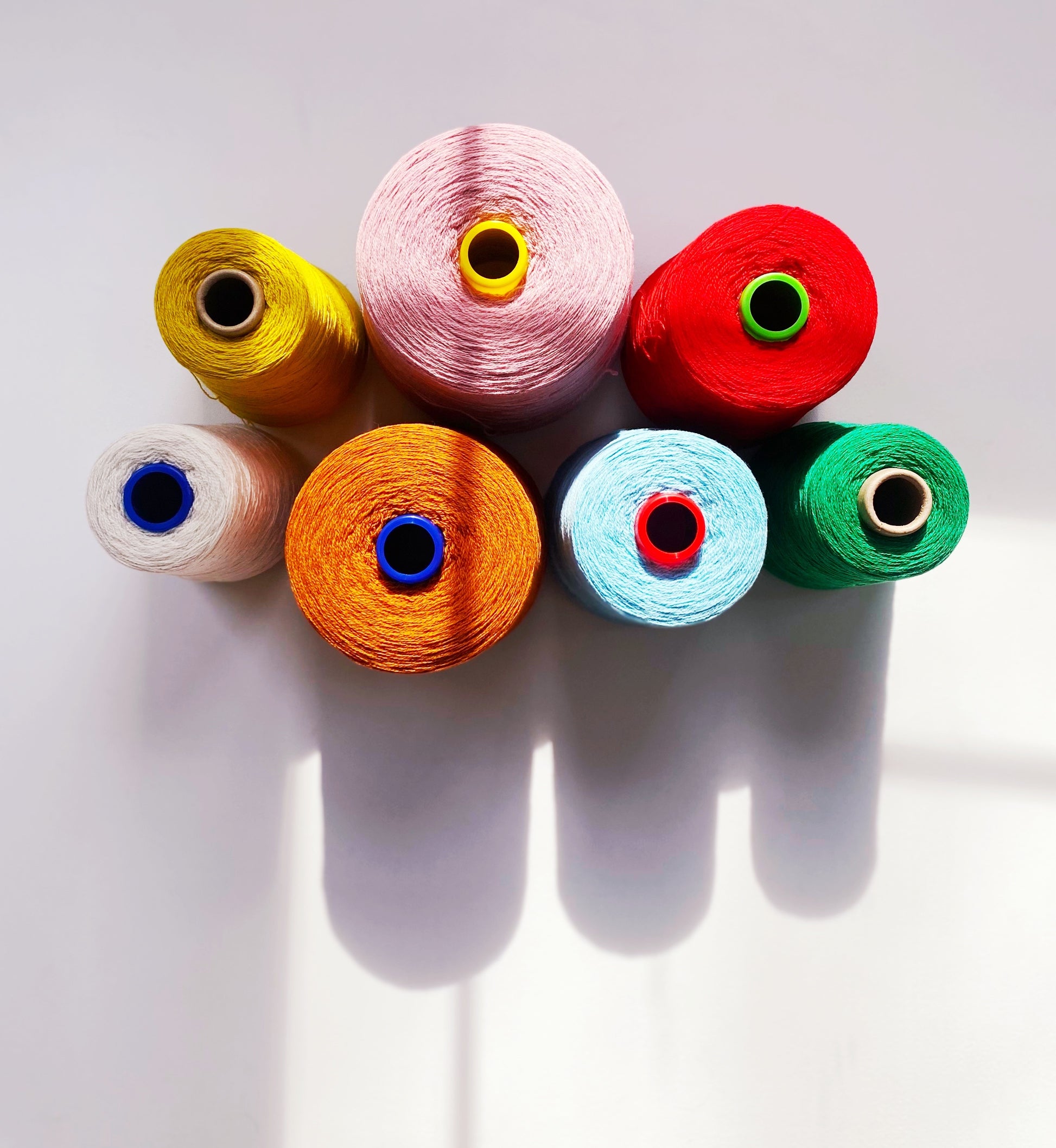 Colorful spools of yarn arranged in a circular pattern on a white background
