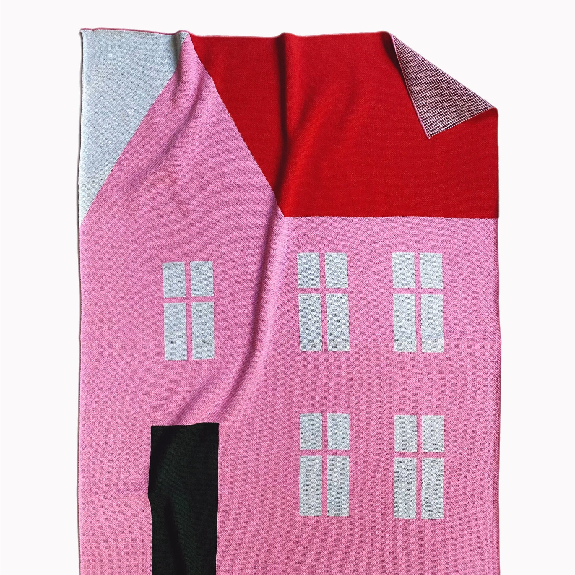 Pink knitted blanket shaped like a house with a red roof on a white background