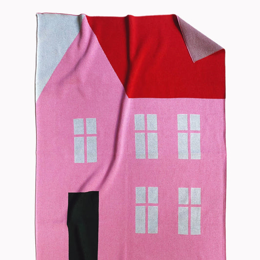 Pink knitted blanket shaped like a house with a red roof on a white background