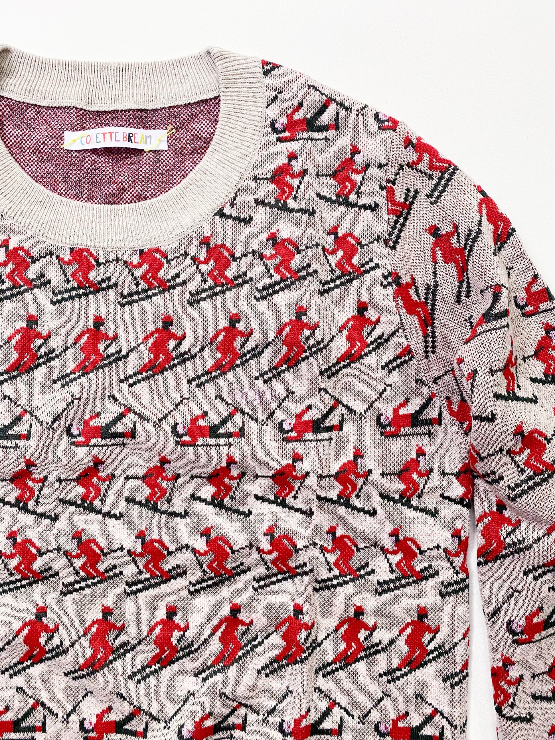 Sweater with red and black pattern of people skiing on a gray background