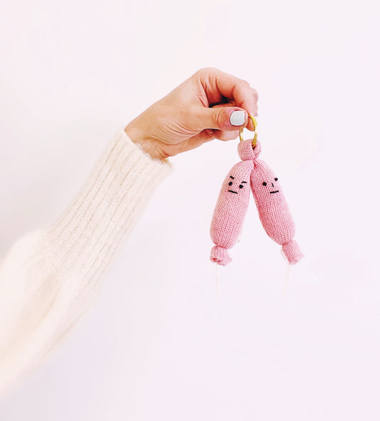 Hand holding a small pink knitted sausage links toy with a neutral background