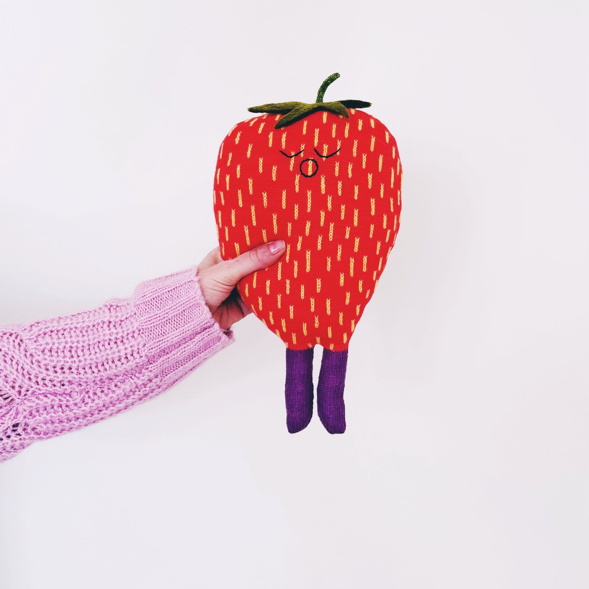 Hand holding a red plush strawberry toy with a white background