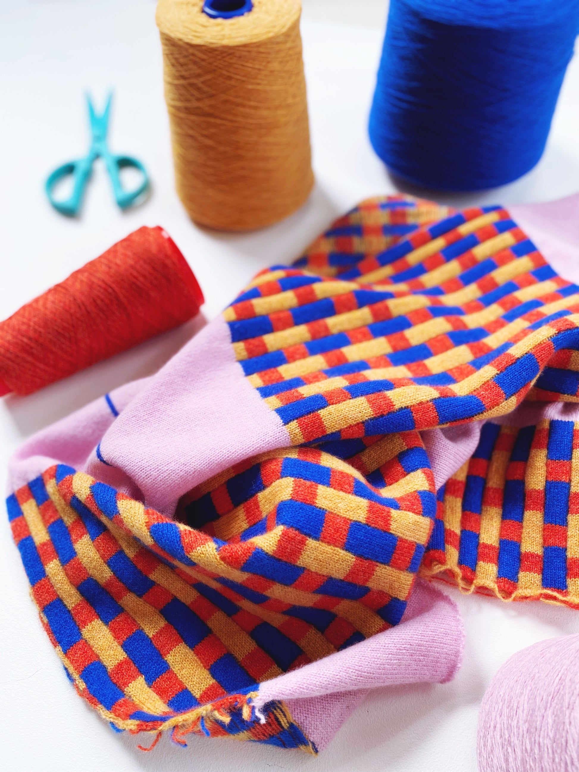 Colorful fabric with a checkered pattern, spools of thread, and scissors on a white background