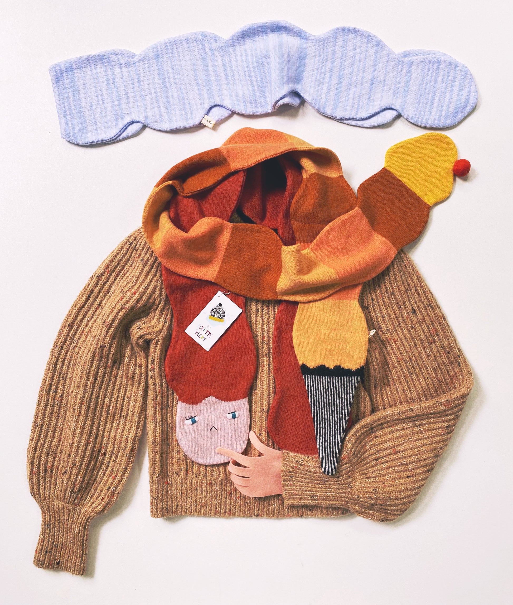 Brown sweater with multiple colorful knitted lambswool scarves wrapped around it on a white background