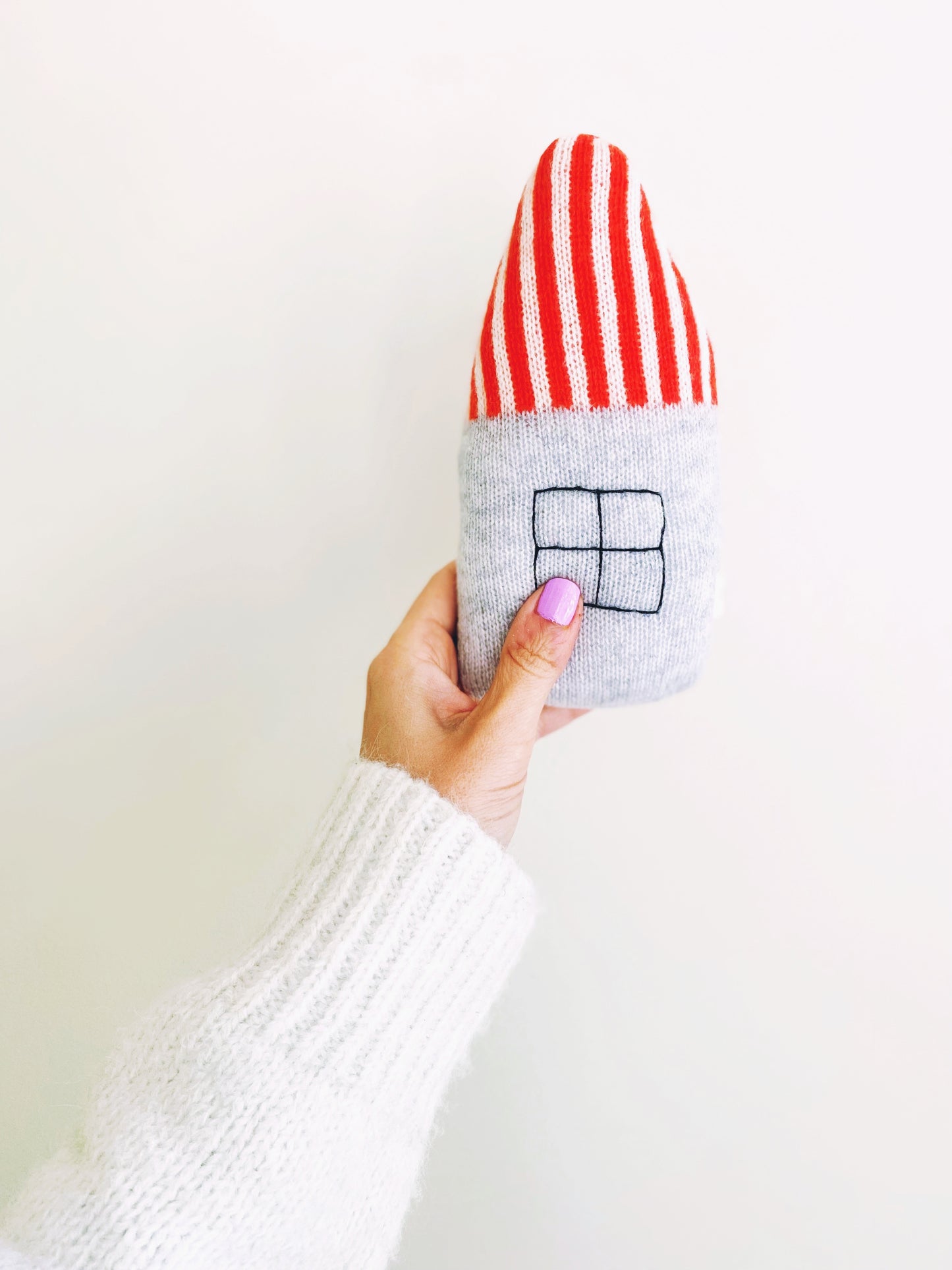 Hand holding a small baby rattle shaoed like a house with a white background