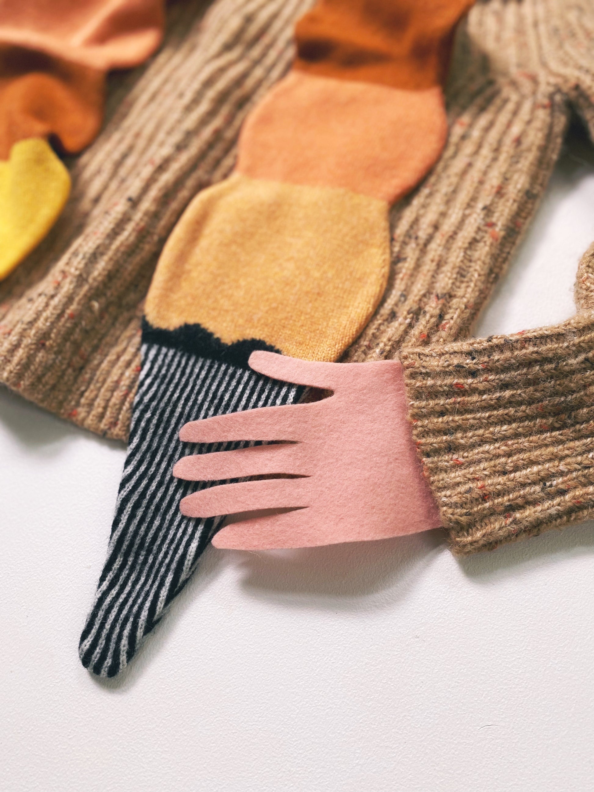 Close-up of a hand holding a colorful knitted lambswool scarf shaped like an ice cream on a white background