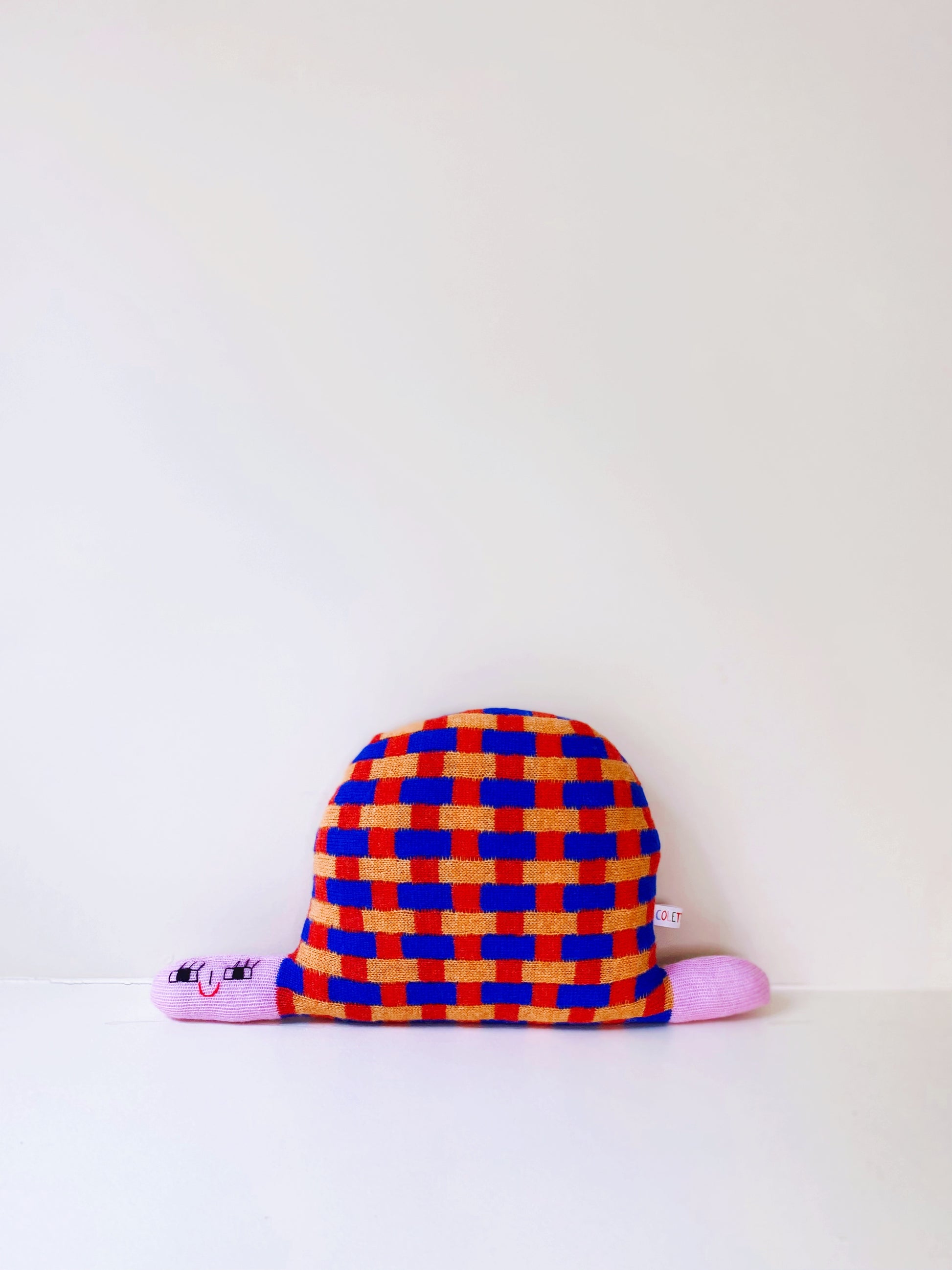 Colorful checkered soft knitted turtle plush toy with pink accents on a white background