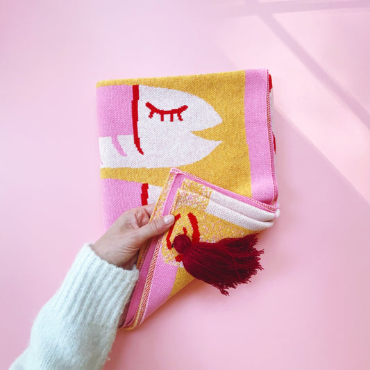 Hand holding a colorful knitted fabric with sardines fish design on a pink background