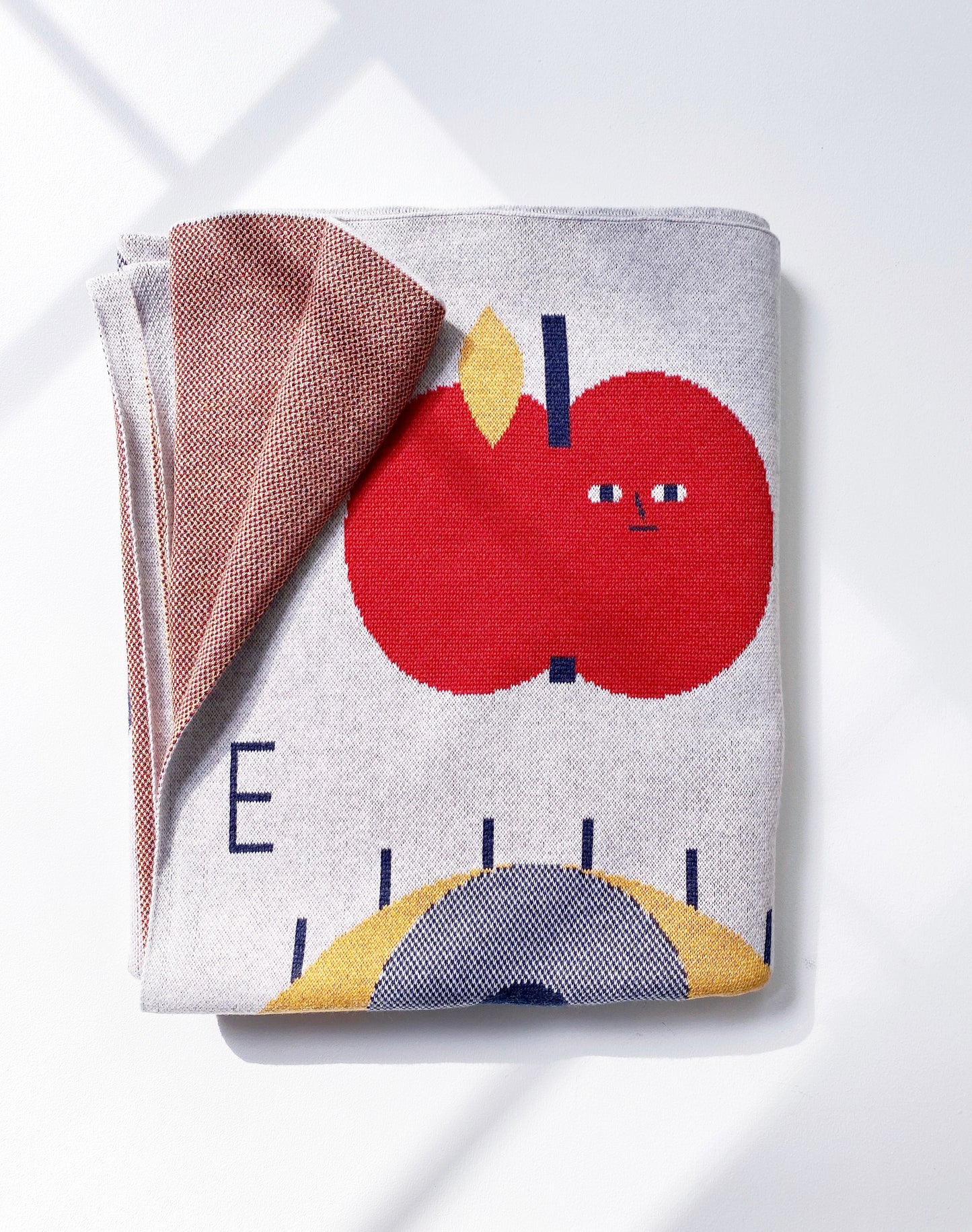 Folded knitted alphabet throw blanket with a red apple design on a white background