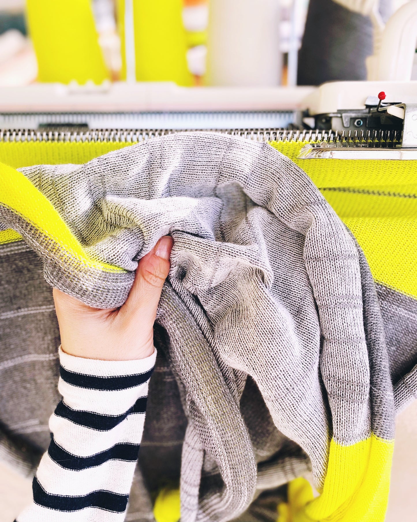 Person holding a gray knitted fabric with a yellow detail in the background
