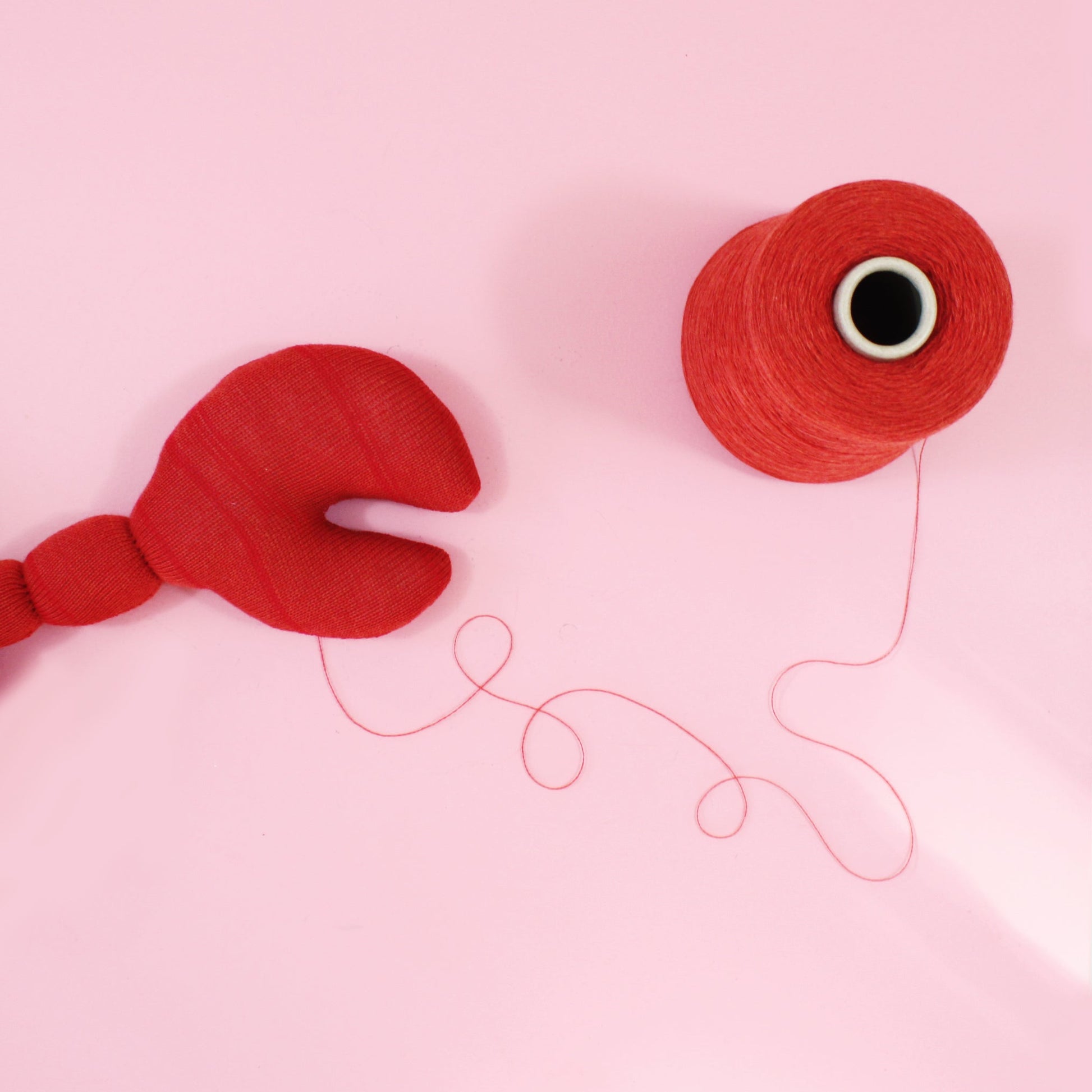 Red yarn ball and spool on a pink background