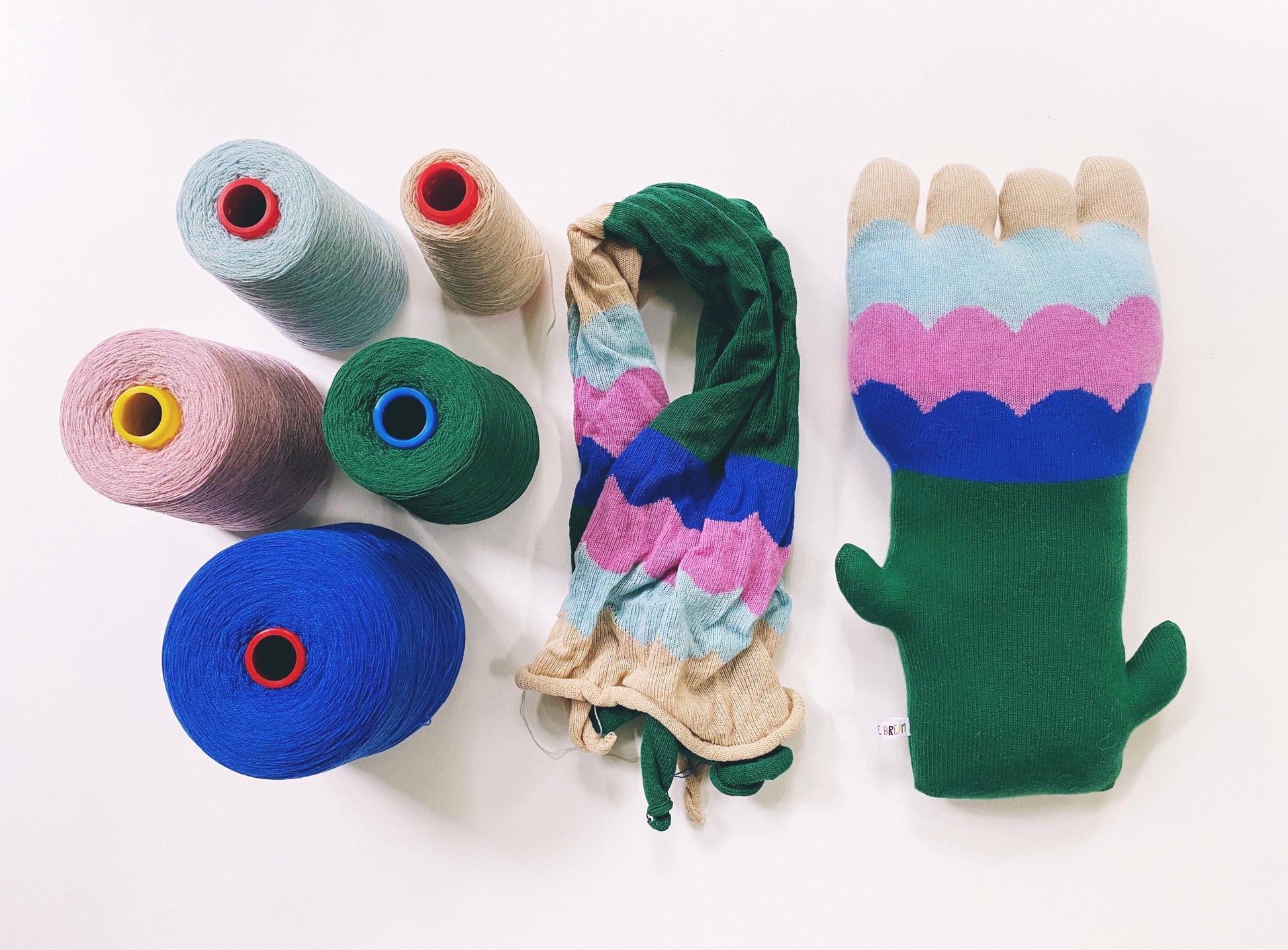Colorful yarn spools and a multicolored flower shaped pillow on a white background