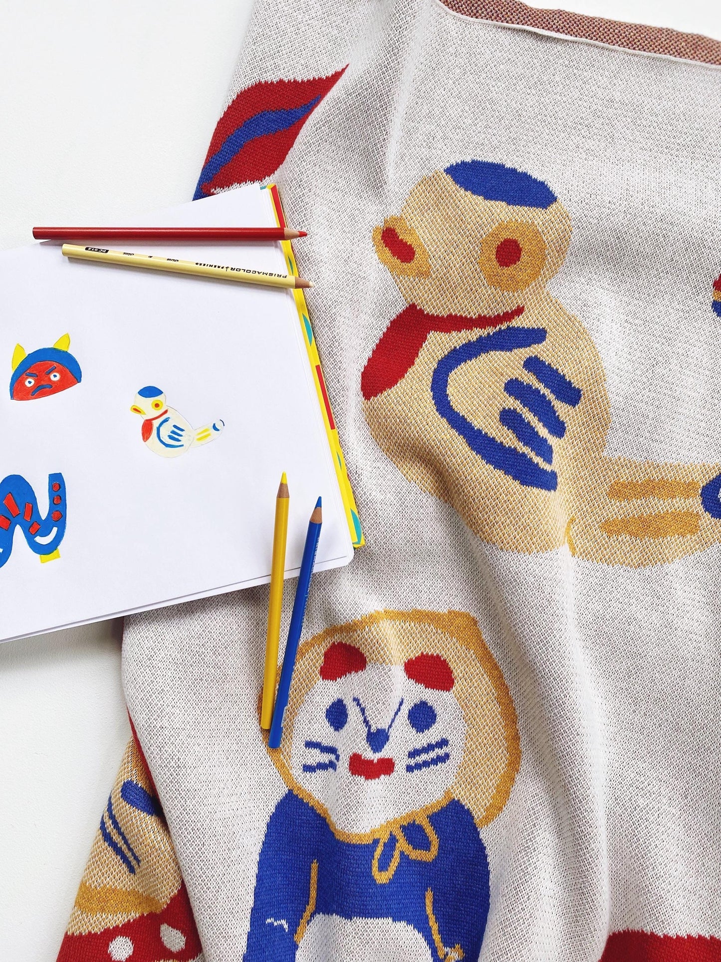 Knitted textile with Japanese folk toys designs and colorful pencils on a white surface