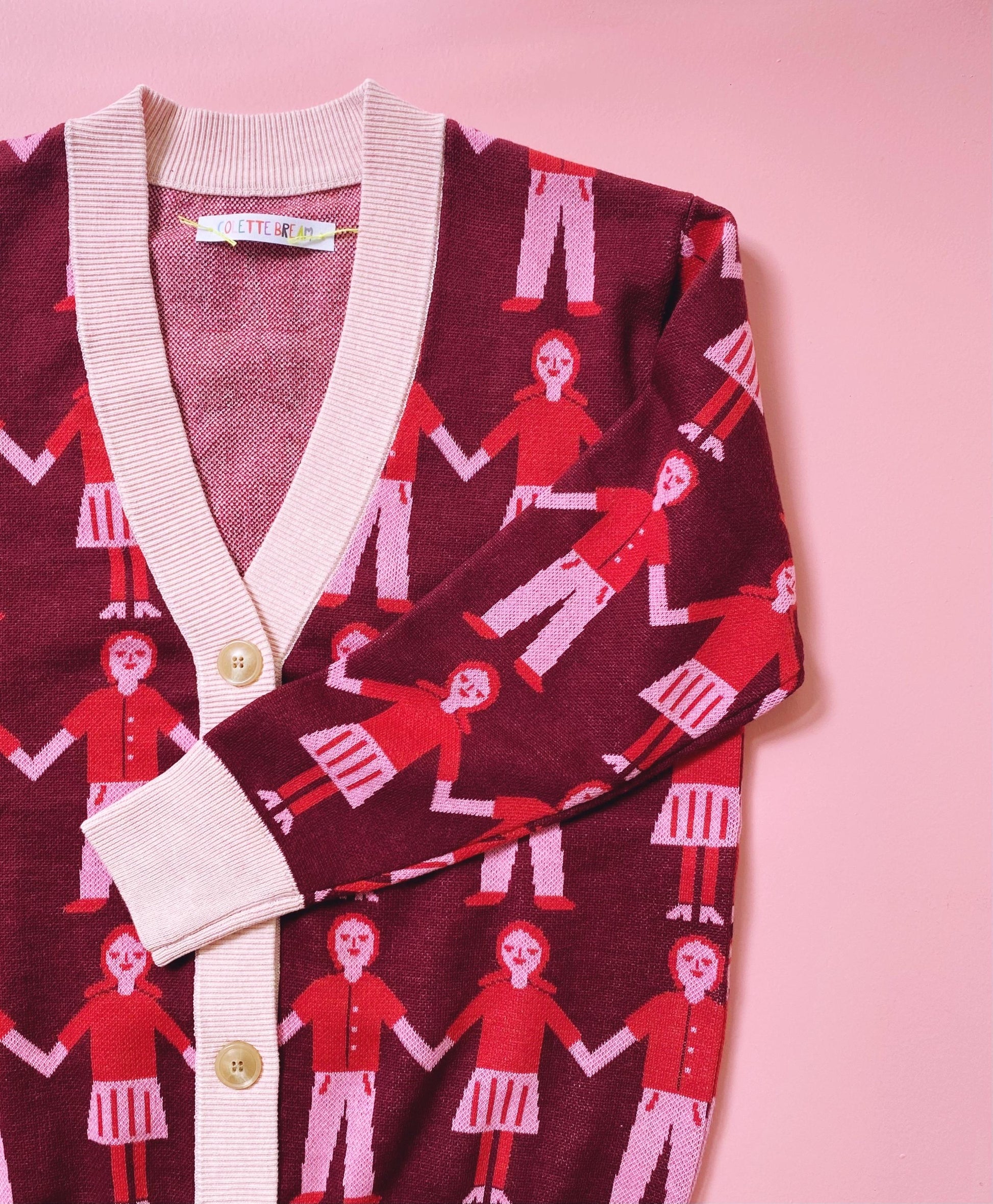 Cardigan with red and white pattern of people holding hands on a pink background