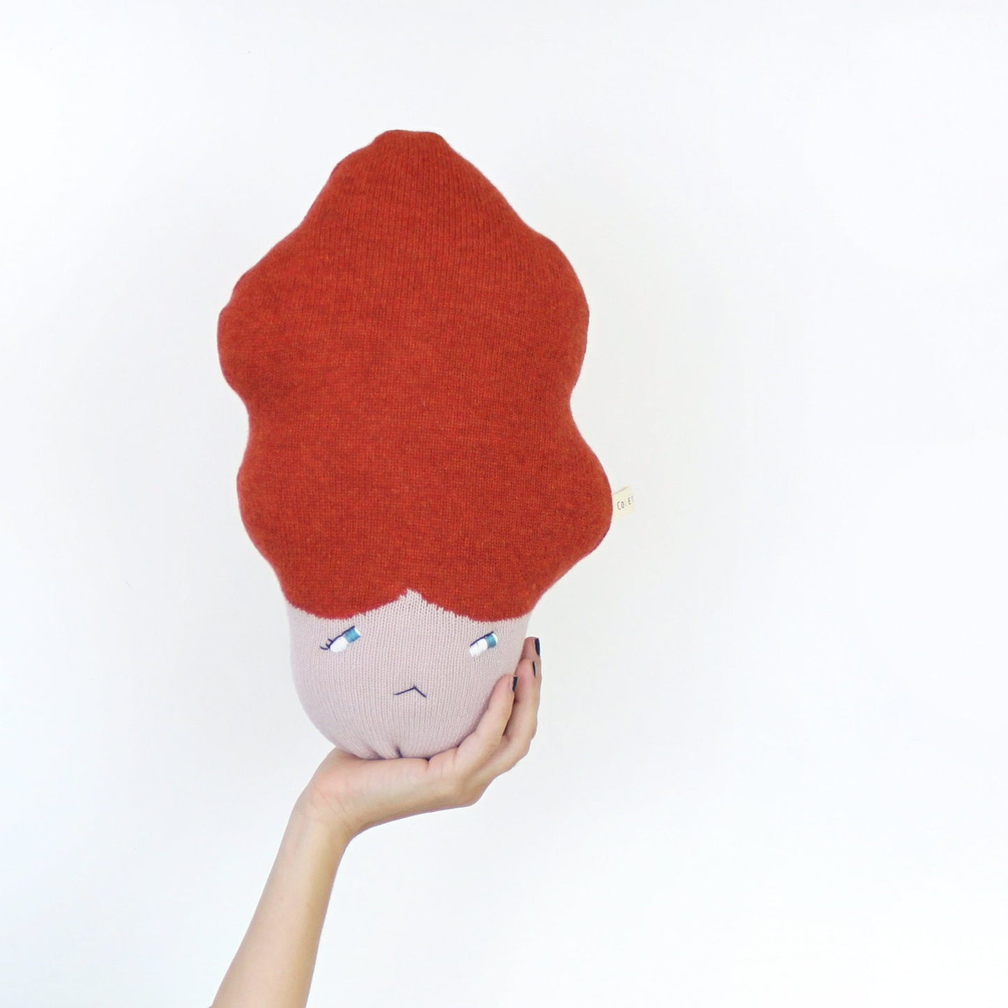 Plush toy with red hair held by a hand against a white background