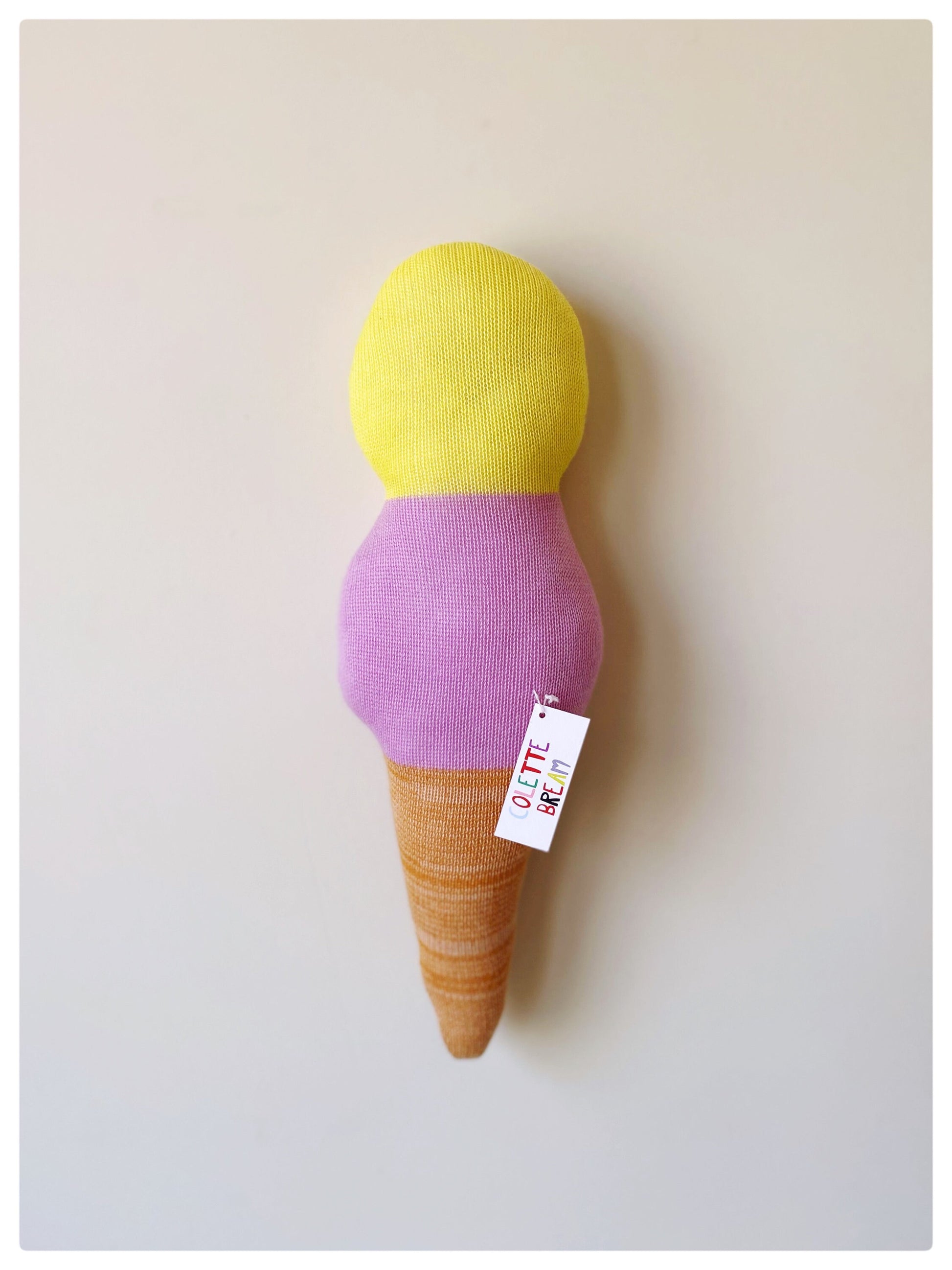 Toy ice cream cone with yellow top, purple middle, and brown base on a light gray background