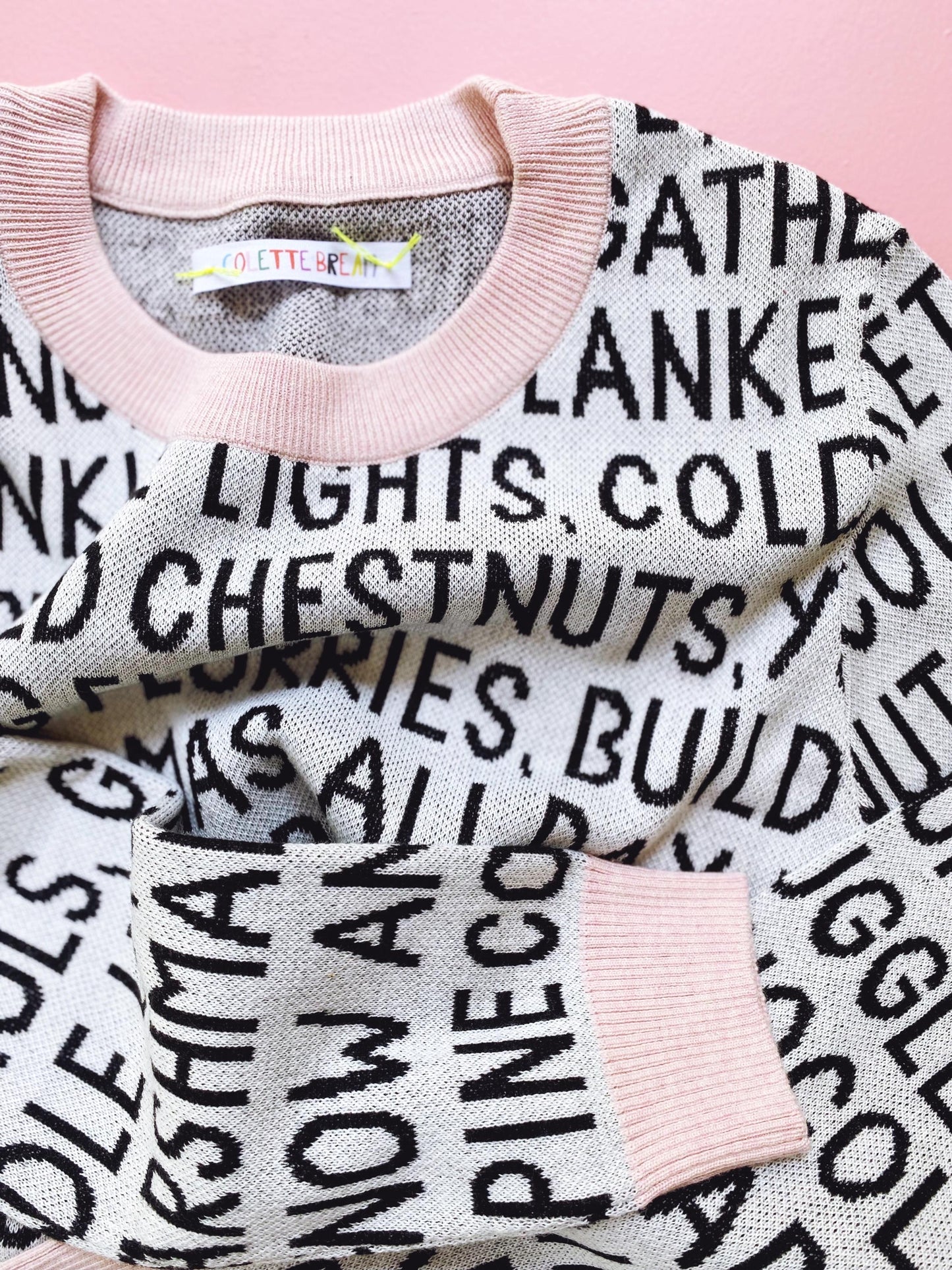 Knitted sweater with black christmas text pattern on a pink background