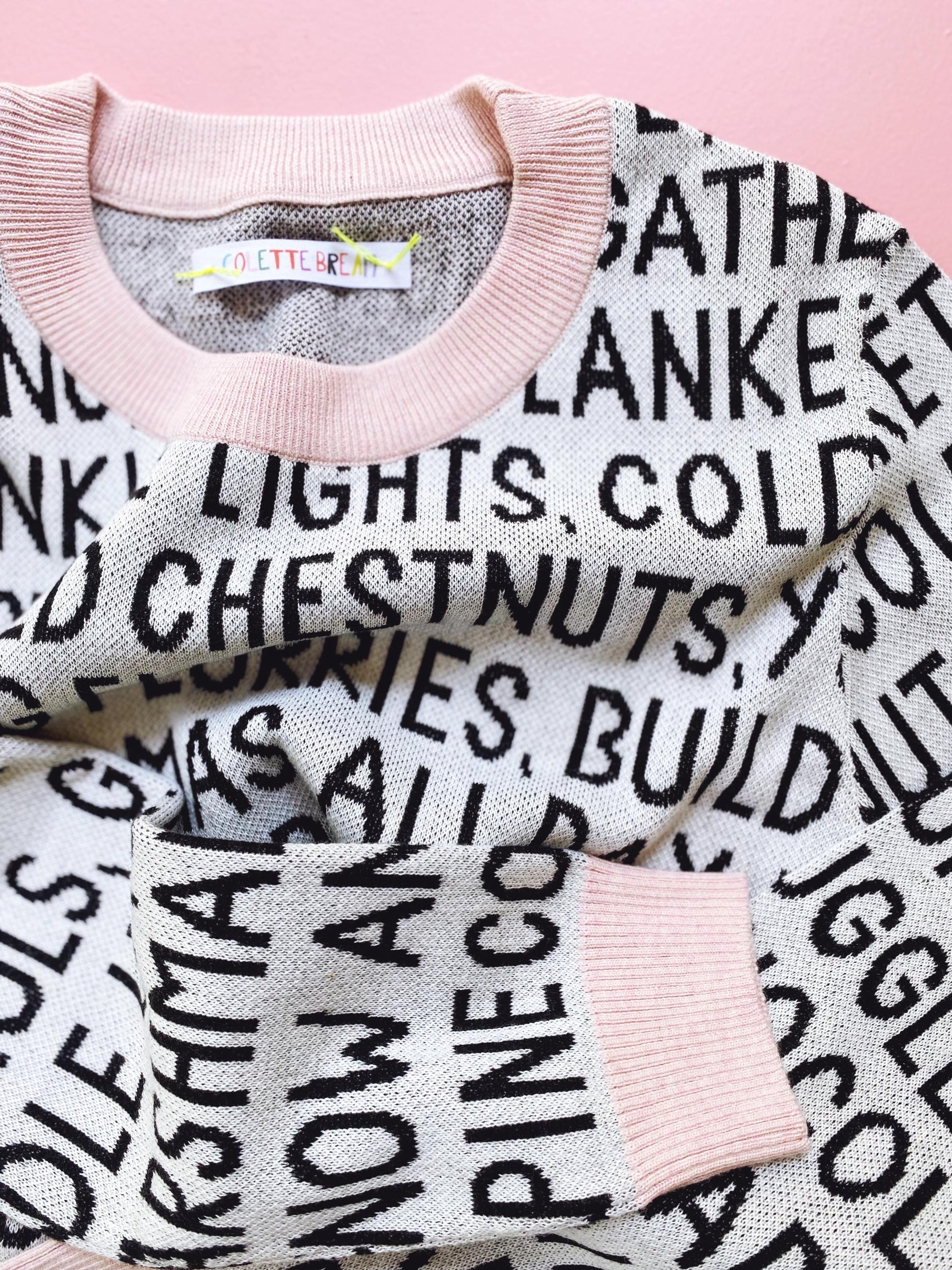 Knitted sweater with black christmas text pattern on a pink background