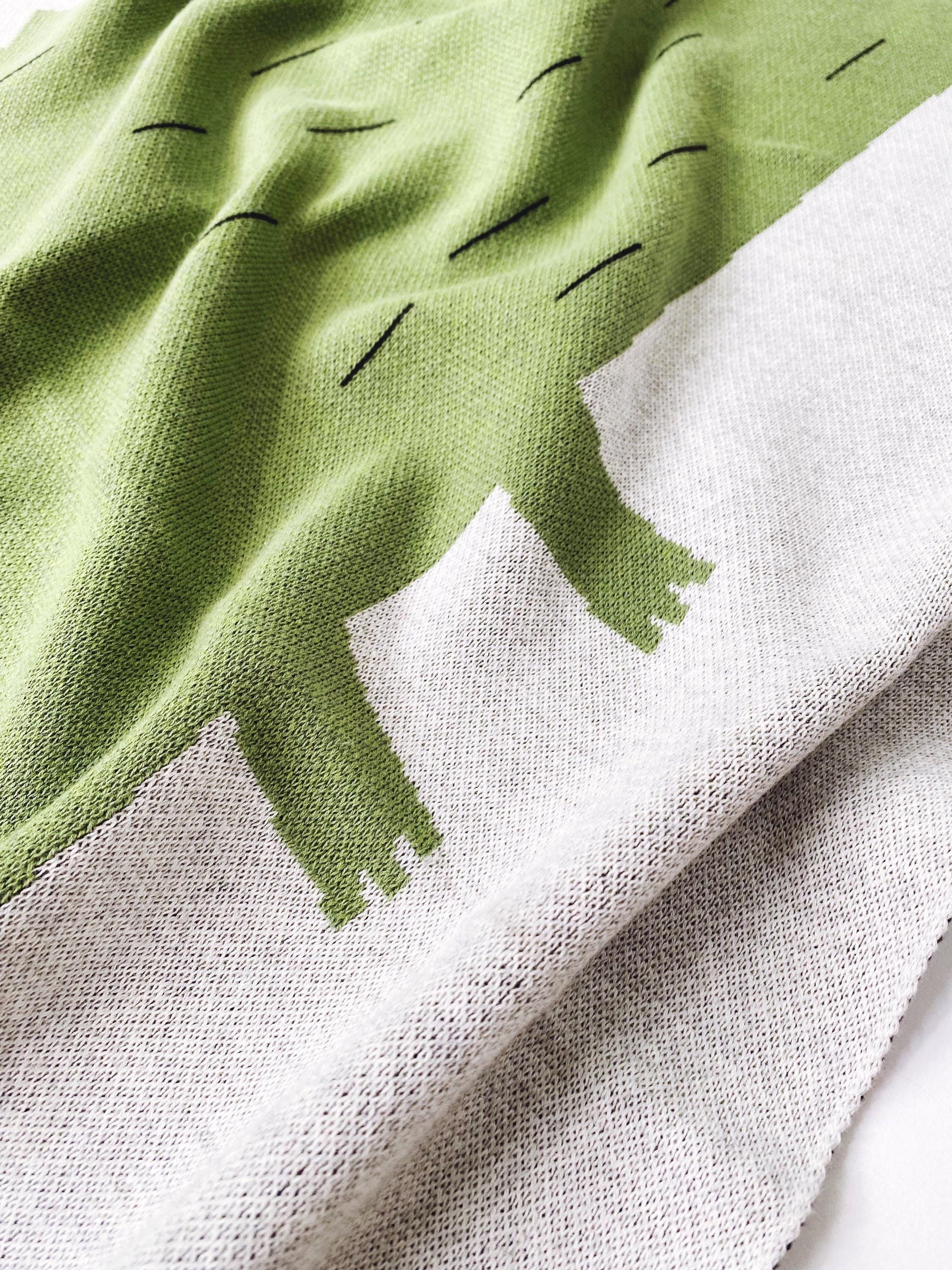 Close-up of a knit fabric with detail of a green alligatordesign on a white background