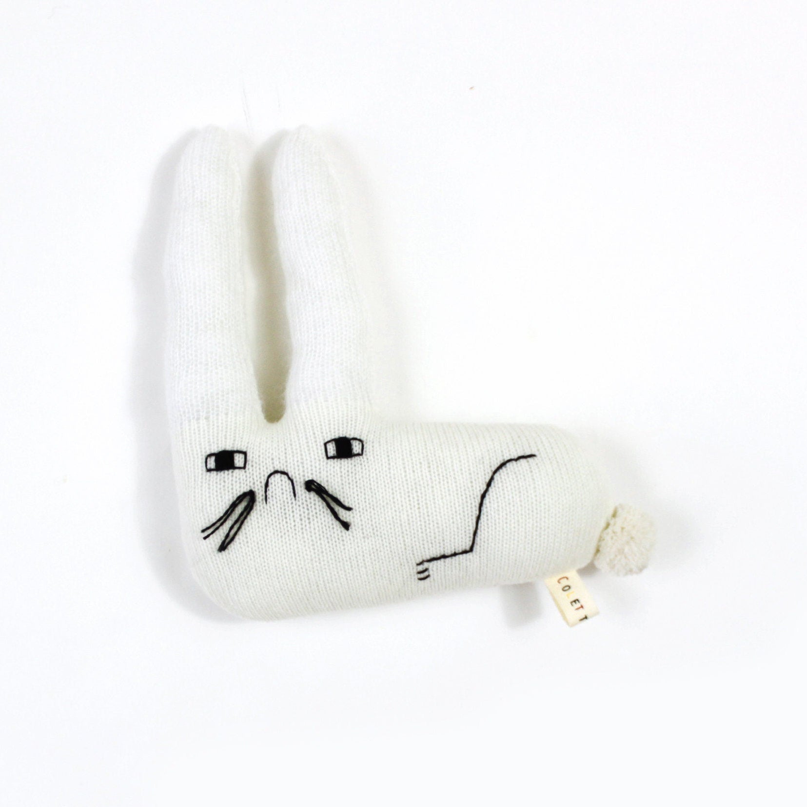 White knitted bunny plush toy with sad face design on a white background