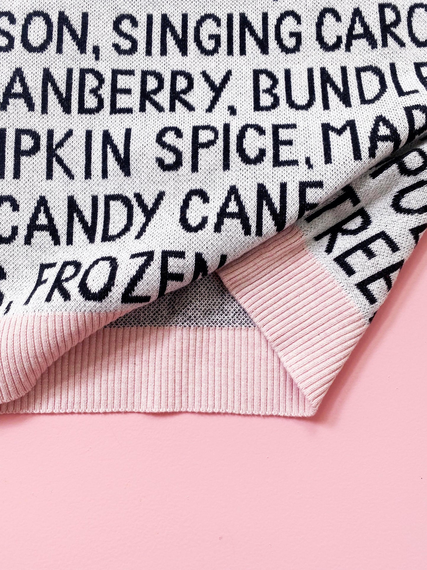 Knitted sweater with black festive christmas text on a pink background