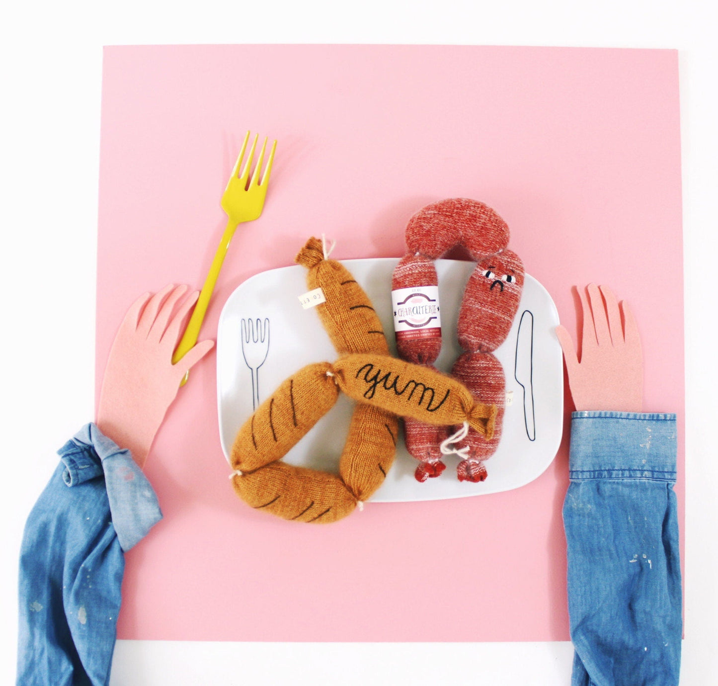 Knitted plush toy sausages on a plate with a pink background
