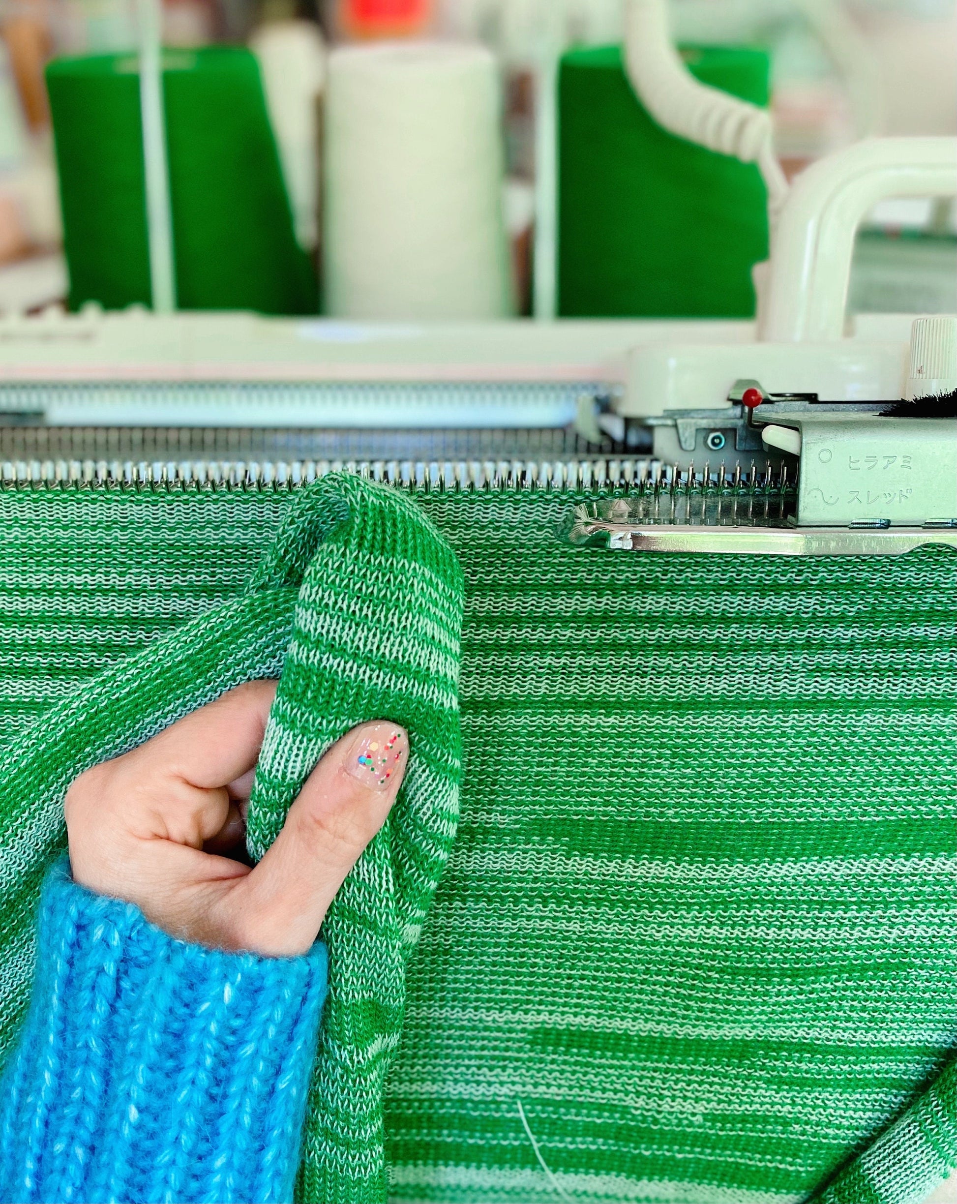Green fabric being held up next to a knitting machine in a textile factory.
