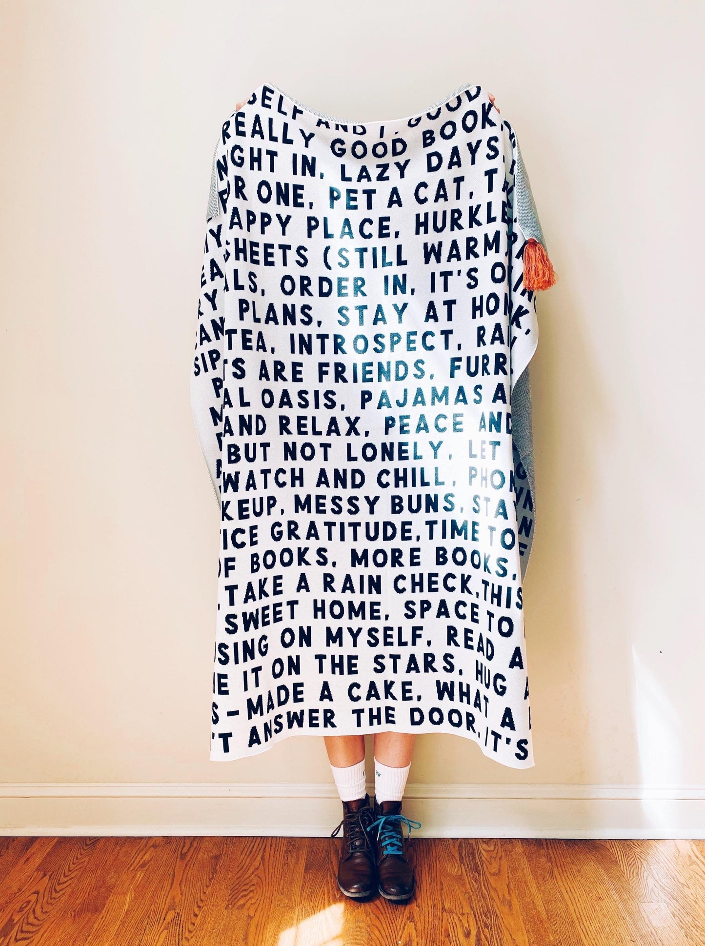 Person holding a large knit throw blanket with text against a plain wall.