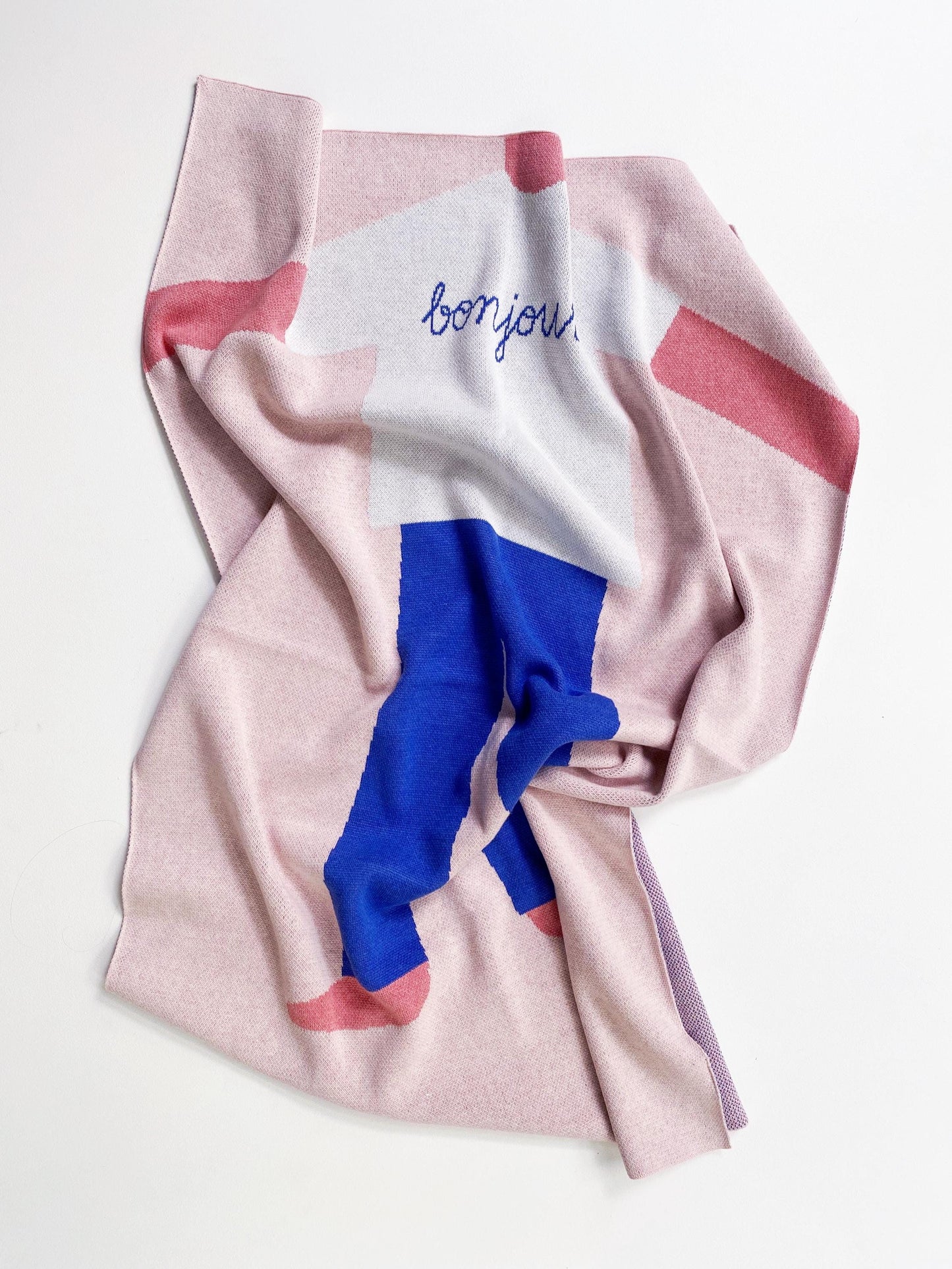 Folded pink knit blanket with a cartoon boy character wearingblue pants and 'bonjour' text on a white background
