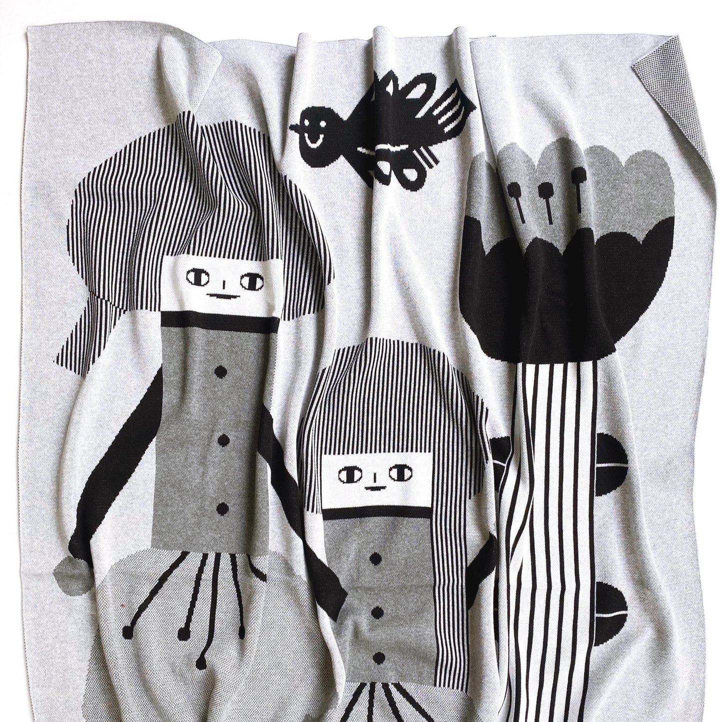 White blanket with black and gray abstract designs of flower andpeople and a bird.