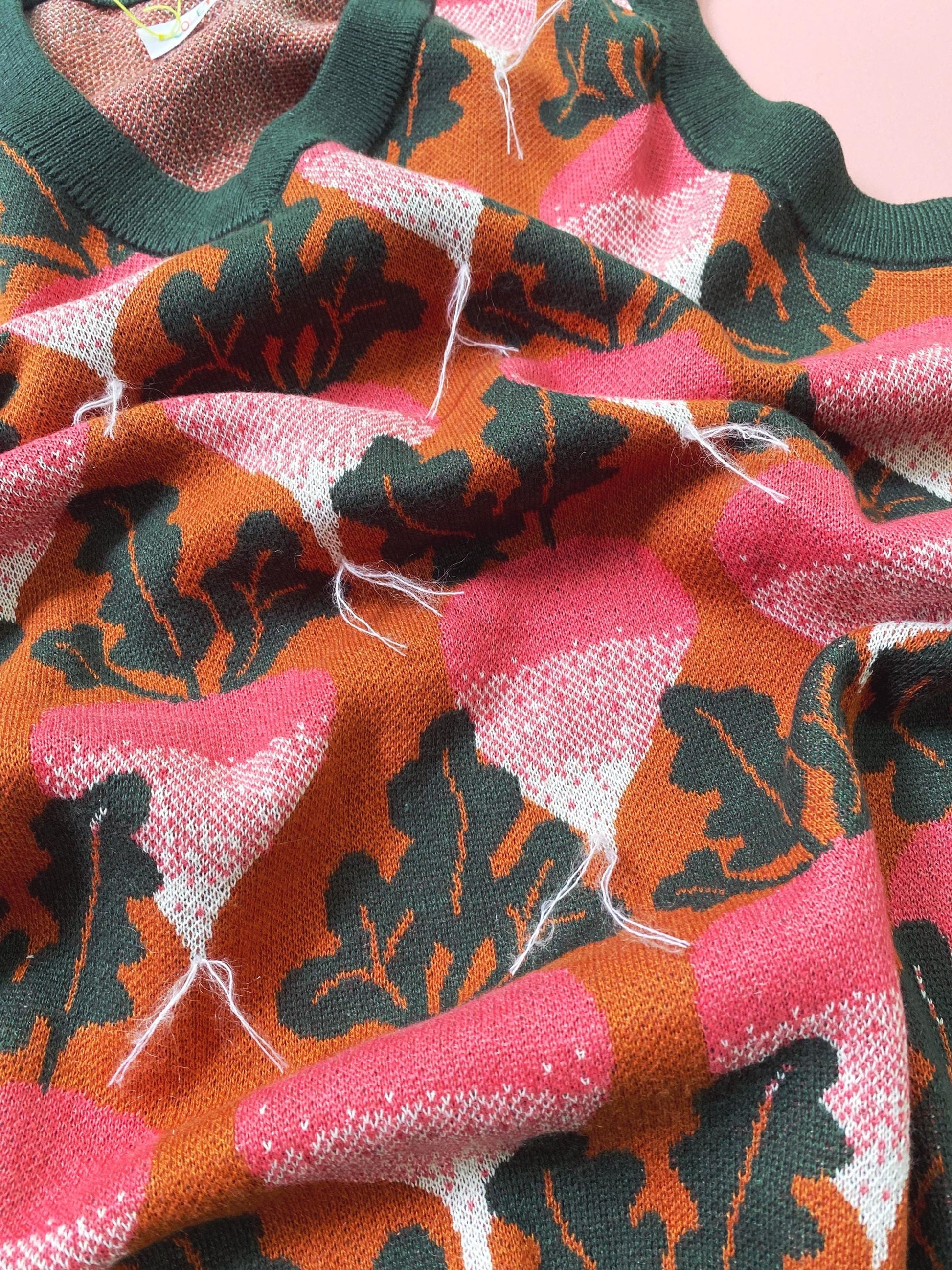 Close-up of patterned fabric, knitted sweater vest with pink, orange, and black beets radish design.