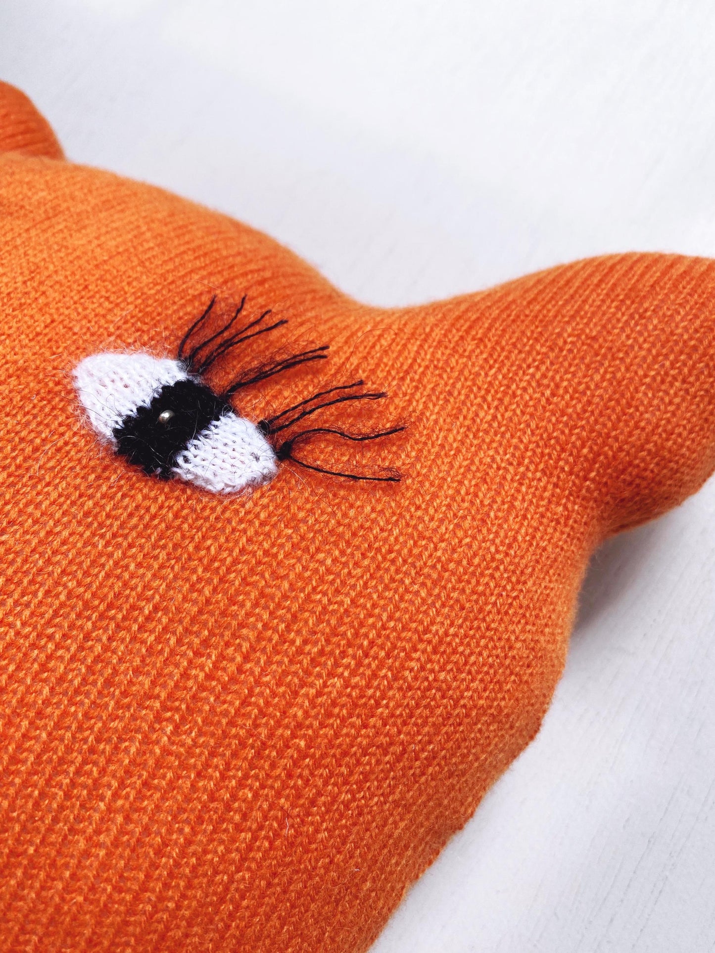Close-up of an orange knitted fox toy with a detailed eye on a white background