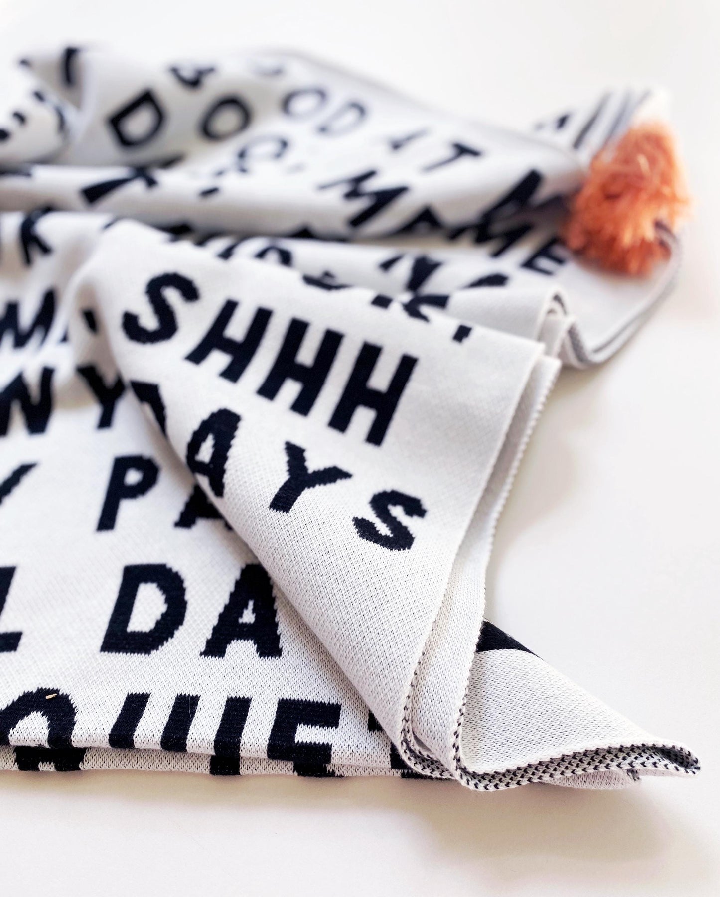 Folded knitted blanket throw with black text on a white background