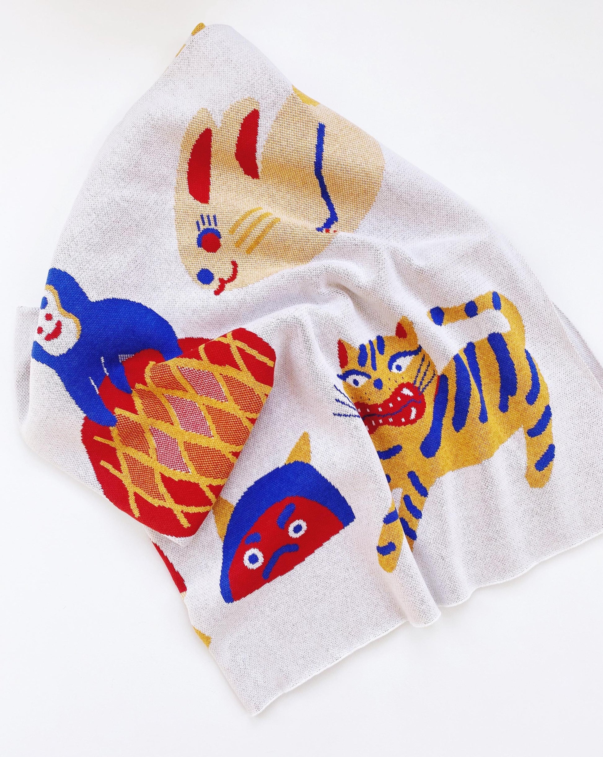 White knitted blanket with colorful tiger illustrations and other japanese characters on a white background