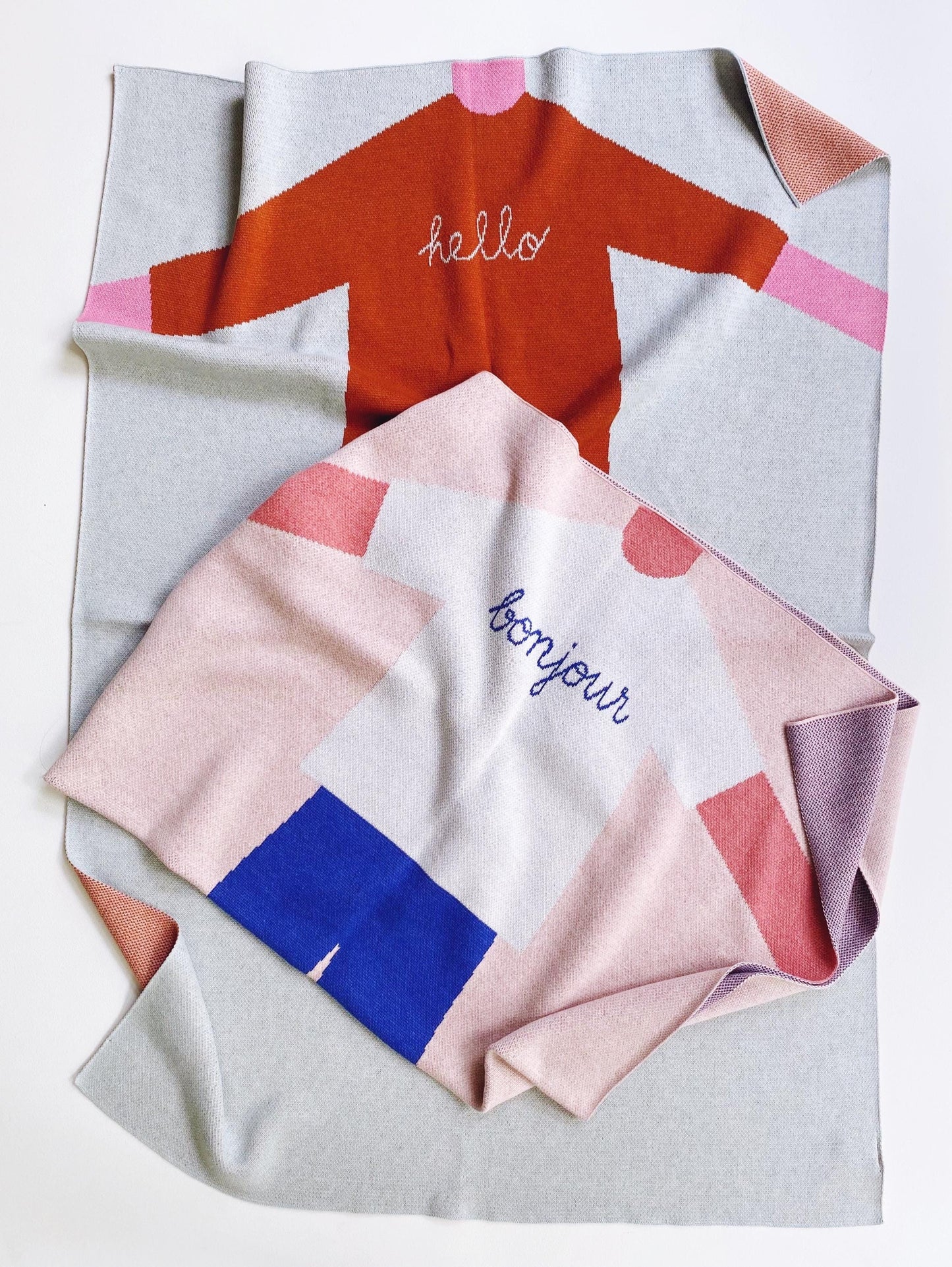 Folded knit baby blanket fabric with colorful patterns and text on a light gray background