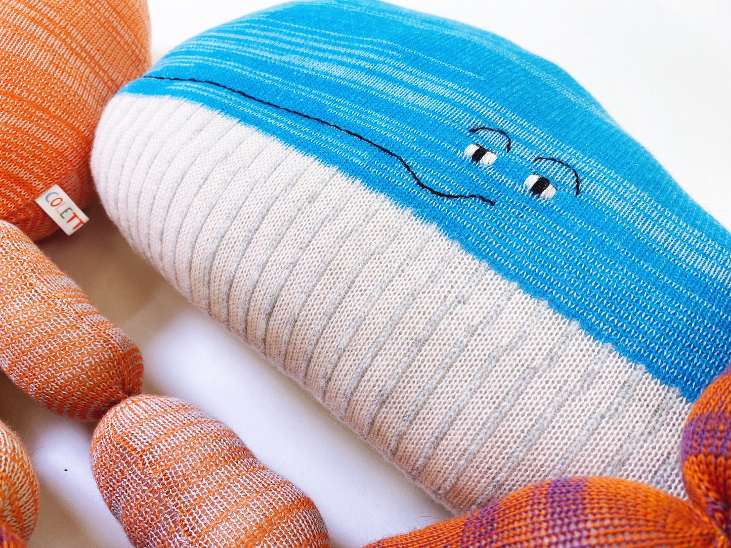 Close-up of a colorful knitted pillow with cartoon face design on a white background