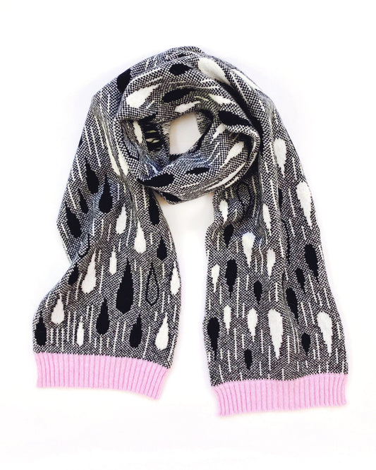 Knitted lambswool scarf with black and white raindrop pattern and a pink trim on a white background