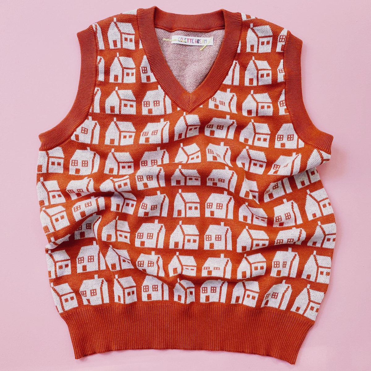 Orange sweater vest with white house pattern on a pink background