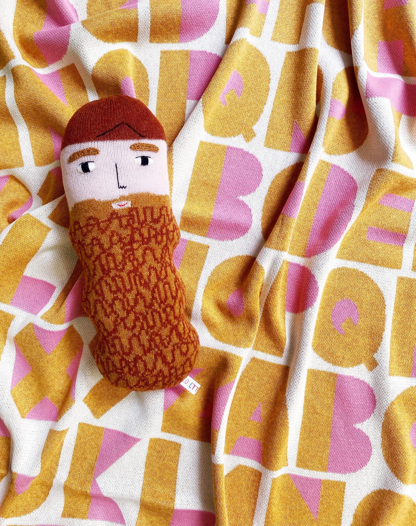 Knitted plush toy with a face and a beard design on a alphabet patterned blanket background