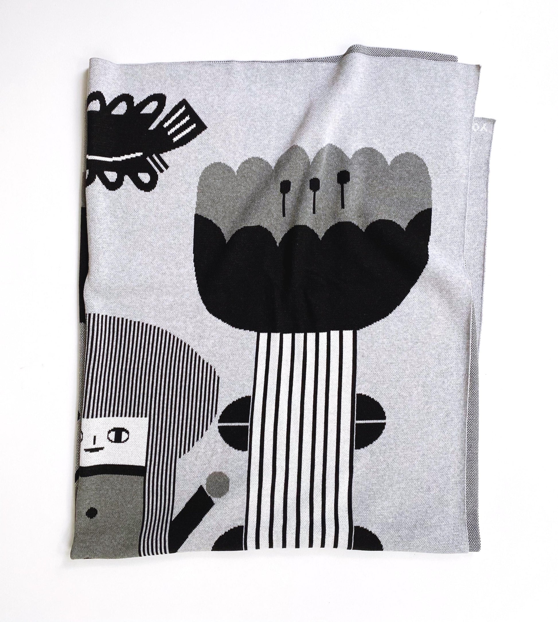 Gray knitted blanket folded with black and white abstract design and flower on a white background