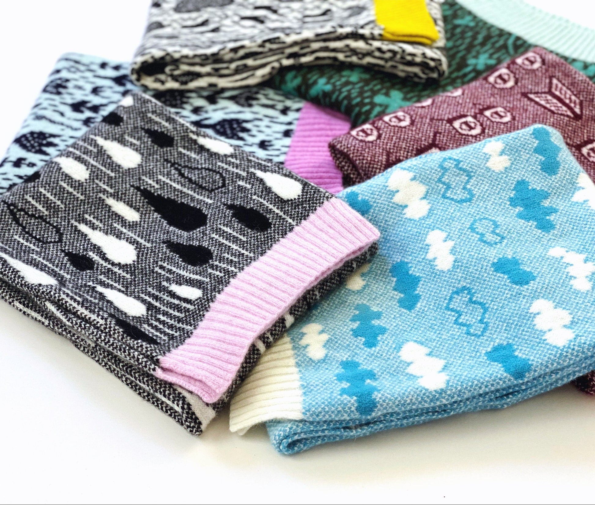 Folded patterned knitted scarves in various colors on a white background