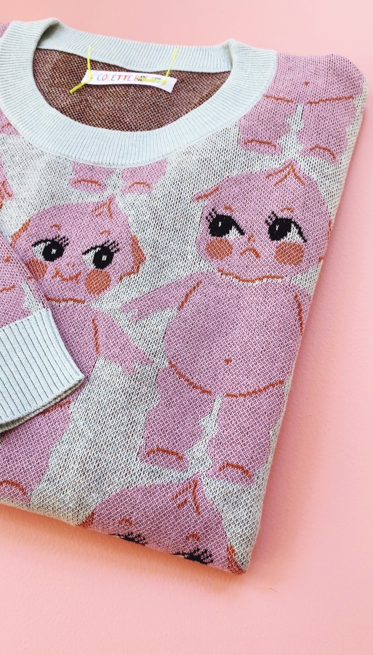Pink knit sweater with cartoon kewpie design on a pink background