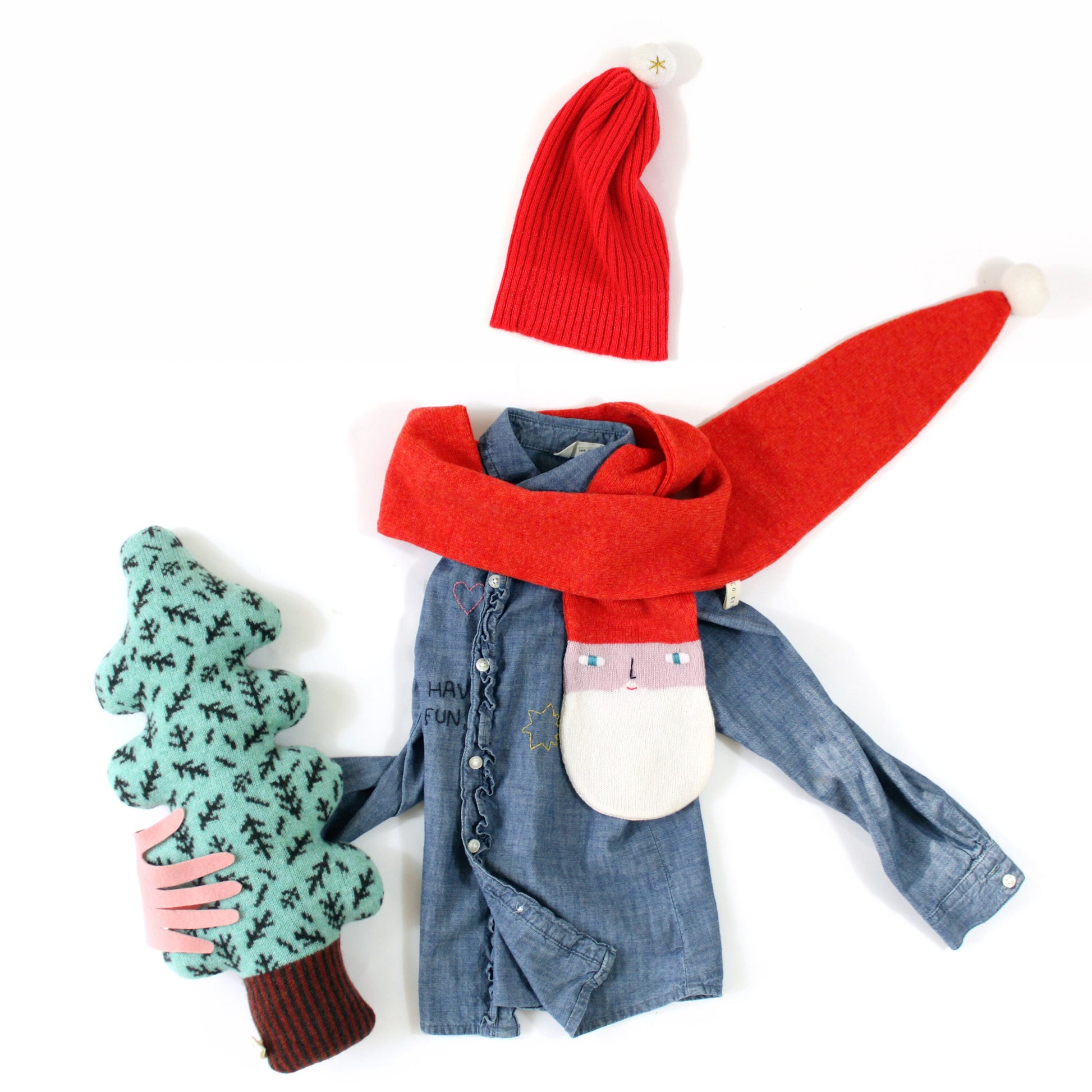 Set of winter clothing including a denim jacket, red santa scarf, red beanie, and green tree shaped pillow on a white background.