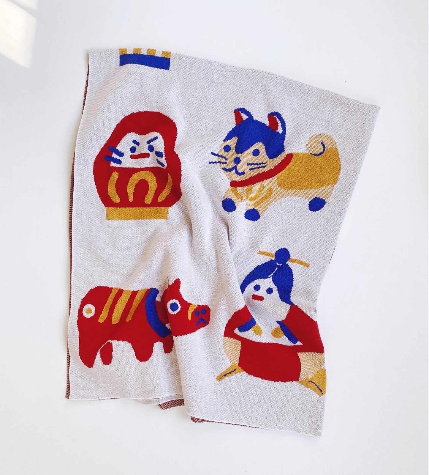 Folded knit blanket with colorful animal designs and other japanese characters on a white background