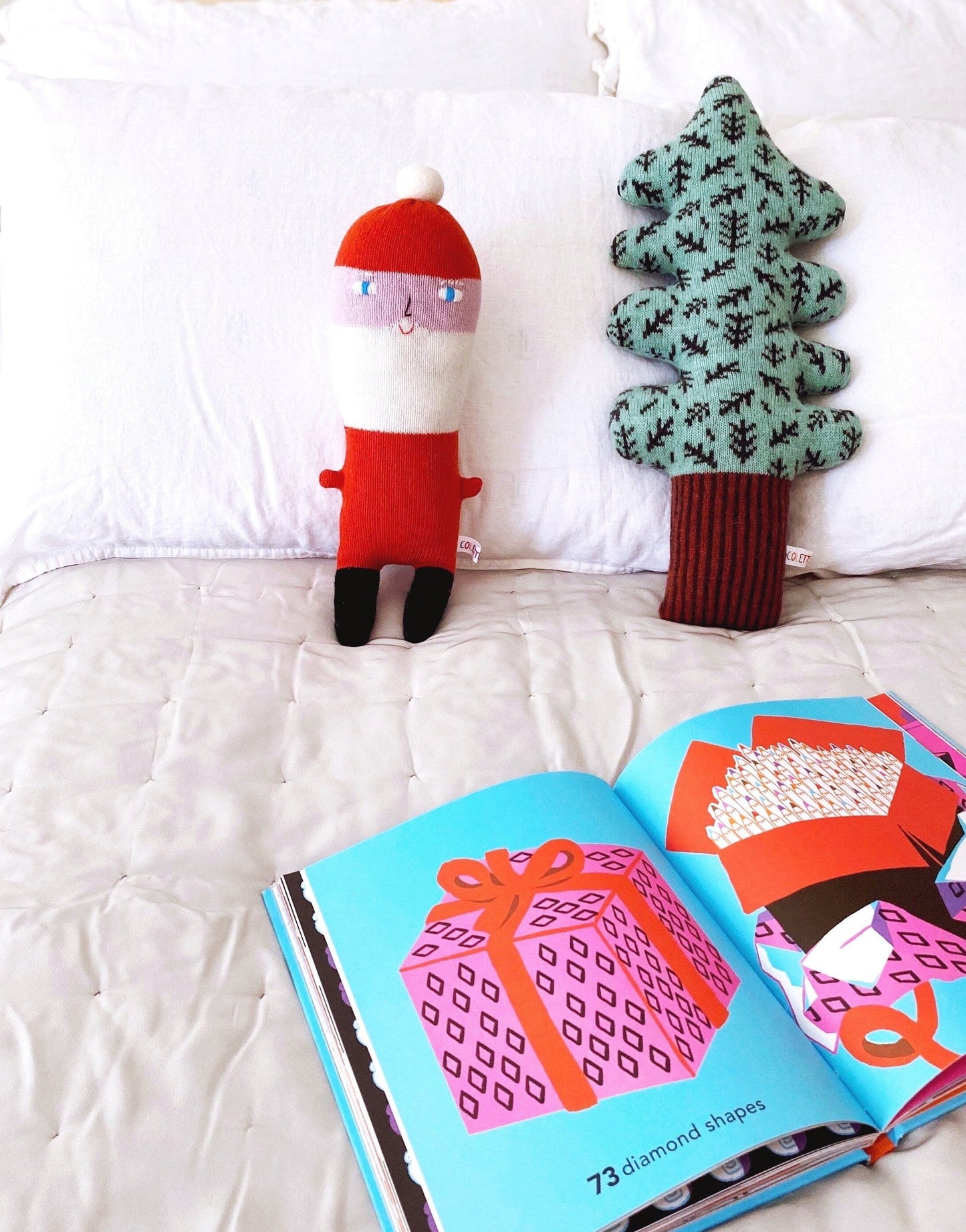 Santa plush toy and tree-shaped pillow next to an open book on a white surface