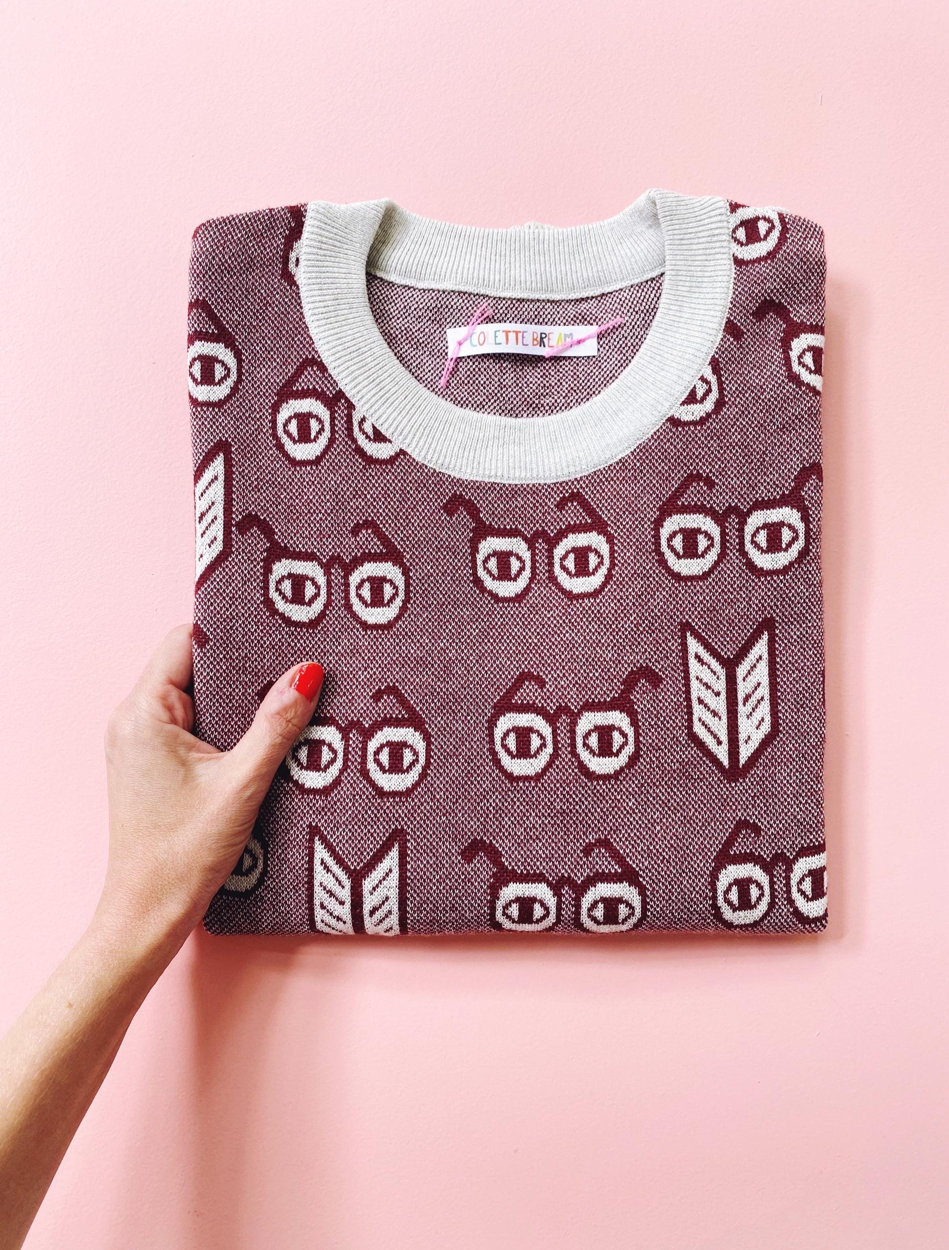 Folded sweater with a spectacles eyeglasses pattern held by a hand on a pink background