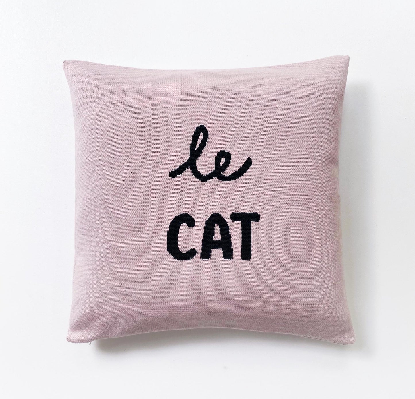 Pink knitted pillow with 'le cat' text on a white background