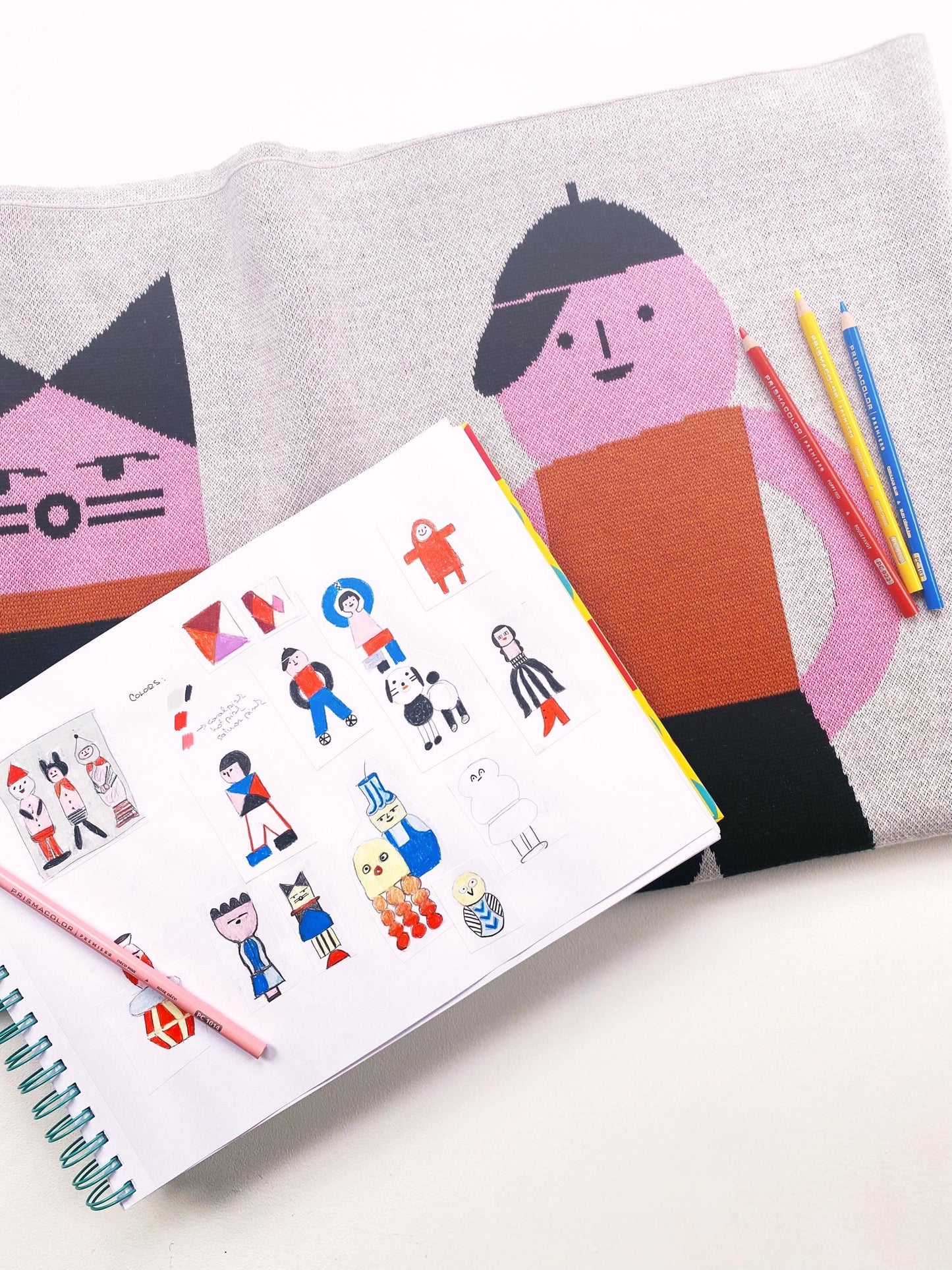 Sketchbook with illustrations of people, pencils, and a pillow with a cat design.