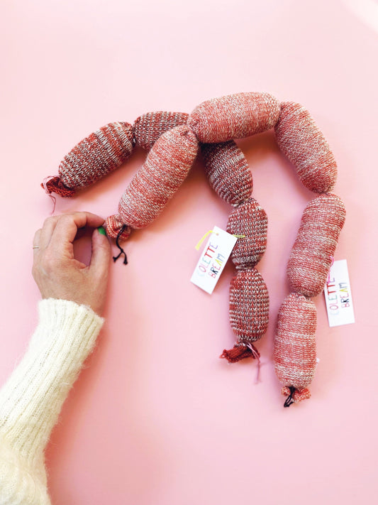 Person arranging knitted sausages on a pink background